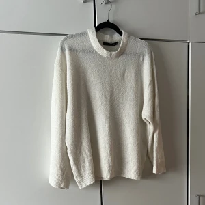 Vit stickad tröja  - Klassisk vit stickad tröja med rund halsringning och långa ärmar. Tröjan har en avslappnad passform och ribbstickade muddar vid hals, ärmslut och nederkant. Perfekt för lager-på-lager och enkel att matcha med olika outfits.