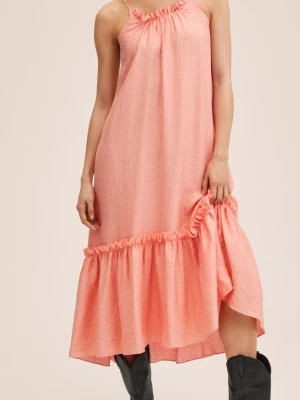 Ljuscoral volangklänning med smala band - Säljer en ljuscoral långklänning med smala axelband och volangdetaljer vid halsringning och nederkant. Klänningen har en lös passform och är tillverkad i ett mjukt bomullstyg som känns luftigt och skönt. Perfekt för varma dagar!