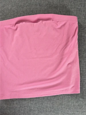 Rosa ribbad bandeau tubtopp Vero Moda - Säljer en rosa ribbad bandeau tubtopp från Vero Moda. Toppen är axelbandslös och har en tight passform med stretchigt material som sitter snyggt på kroppen. Perfekt att styla med jeans eller kjol för en trendig look.