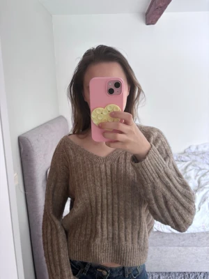 Stickad tröja - Säljer en beige ribbstickad tröja med v-ringning och croppad passform. Tröjan har långa, lite vidare ärmar och är perfekt för lager på lager. Materialet ser mjukt och mysigt ut, perfekt för kyligare dagar.