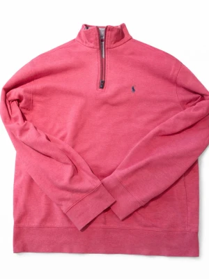 Rosa half-zip tröja från Polo Ralph Lauren - Snygg rosa tröja med half-zip och hög krage från Polo Ralph Lauren. Tröjan har ett litet blått logobroderi på bröstet och ribbade muddar vid ärmslut och nederkant. Perfekt för en avslappnad men stilren look.