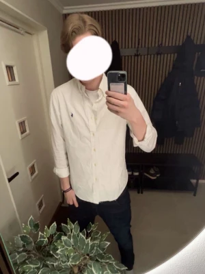 Vit skjorta från Ralph Lauren - Klassisk vit skjorta från Ralph Lauren med button-down krage och den ikoniska blå logotypen broderad på bröstet. Skjortan har långa ärmar och är tillverkad i ett mjukt bomullstyg. Perfekt till jeans eller chinos för en clean och stilren look.