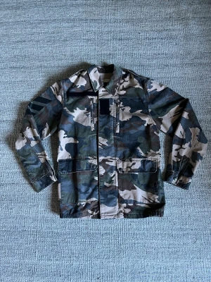 Camouflage vindjacka med dragkedja - Snygg camouflagejacka från Zadig & Voltaire. Jackan har flera fickor. Perfekt för dig som behöver en stilren och unik jacka inför våren. Skicket är superbra - 9/10. Tveka aldrig att fråga om du har någon fundering. Nypris på jackan är ca 400€ ≈ 4000kr. 