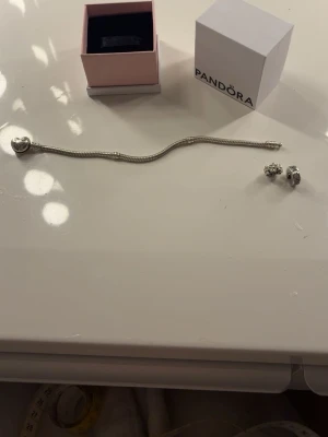 Pandora silverarmband med berlocker - Säljer mitt silvriga armband från Pandora med två  berlocker då jag inte använder silver smycken längre. Armbandet är 16 centimeter och tvättat så ser helt nytt ut! Säljer med berlockerna därav priset! ⚠️Endast blommig berlock kvar⚠️