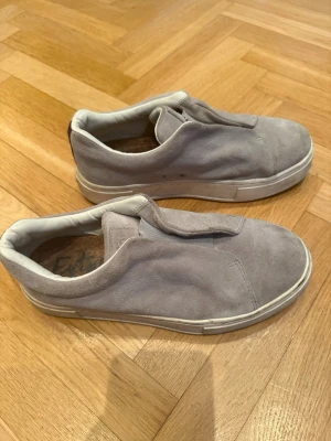 Grå slip-on sneakers i mocka från Eytys - Säljer ett par stilrena grå slip-on sneakers i mocka med vit sula. Skorna har minimalistisk design utan snörning och diskreta ventilationshål på sidan. Insidan är vadderad för extra komfort och sulan är i gummi. Perfekta för en clean och avslappnad look.