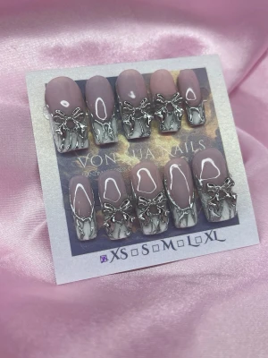 Cyb3R2000 (XS); Medium Square - Snygga handgjorda press-on naglar i en nude rosa nyans med french, handmålad 3D chrome nailart. Naglarna har en medium square form och är dekorerade med detaljerade silverfärgade rosetter och metallisk kant. Perfekt för dig som vill ha en unik och trendig look. XS: 14 mm, 11 mm, 11,5 mm, 10 mm, 8 mm 