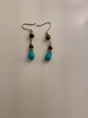 Turk sopärlörhängen med bruna detaljer - Unika handgjorda örhängen med droppformade turkosa pärlor, bruna facettslipade pärlor och gulbruna runda pärlor. Krokar i silverfärgad metall. Perfekta för dig som vill ha färgglada accessoarer med boho-vibe.