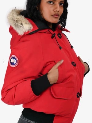 Röd dunjacka från Canada Goose - Riktigt snygg röd dunjacka från Canada Goose med patch på ärmen och stor huva med äkta päls. Jackan har svarta knappar, dragsko vid halsen och praktiska fickor framtill. Perfekt för kalla vinterdagar och riktigt varm.