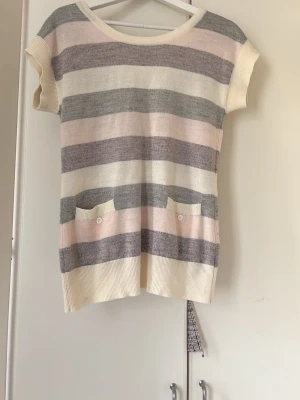 Randig kortärmad kofta i pastell - Kortärmad kofta med breda ränder i ljusgrått, vitt och ljusrosa. Koftan har knappar framtill, två små fickor med knappdetaljer och ribbade kanter. Perfekt för lager på lager och ger en chill vibe till din outfit.