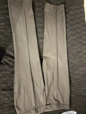 Grå raka kostymbyxor - Snygga grå kostymbyxor med raka ben och pressveck. Byxorna har knäppning och fickor bak med knappdetalj. Perfekta för en stilren look och passar till skjorta eller t-shirt.
