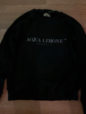 Svart sweatshirt från Acqua Limone - En svart sweatshirt från Acqua Limone med klassisk logga tryckt på bröstet. Tröjan har rund halsringning och ribbade muddar vid ärmslut och nederkant. Perfekt för en avslappnad och stilren look.