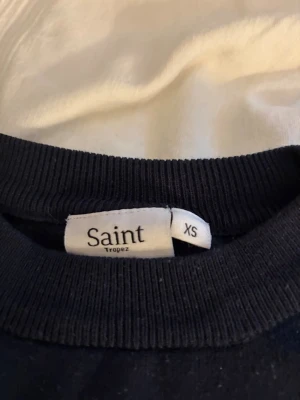Mörkblå topp från Saint Tropez - Mörkblå topp från Saint Tropez med rund halsringning och korta ärmar. Modellen är enkel och stilren med ribbade kanter vid hals och ärmslut. Perfekt att matcha med jeans eller kjol för en clean look.
