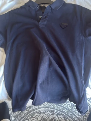 Mörkblå pikétröja med krage Prada slim fit  - Snygg mörkblå pikétröja med klassisk krage och knappar framtill. Tröjan har en diskret patch på bröstet och är tillverkad i ett mjukt bomullsmaterial. Perfekt till jeans eller shorts för en avslappnad look.