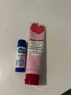 Lypsyl läppbalsam & jordgubb handkräm - Säljer ett Lypsyl Original läppbalsam i blå hylsa och en Milky Drop Strawberry Hand Cream i rosa tub med jordgubbsmotiv. Perfekt för att återfukta både läppar och händer. Handkrämen har söt design och doft av jordgubb.
