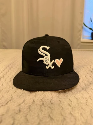 New Era 59FIFTY Fitted - Den här svarta New Era Chicago White Sox-kepsen har en unik design med ett rosa hjärta bredvid lagets logotyp. Den är i bra skick men finns nån fläck på inner skärmen.