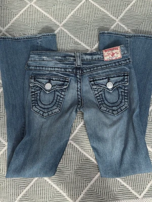 Lågmidjade bootcut true religion jeans  - Ett par joey big t lågmidjade true religion jeans som är i storleken 25w men sitter som en 26w. Midjemått = 38cm och innerbensläng ligger på 79cm. Säljer eftersom dem inte kommer till användning längre och rensar min garderob. Mycket bra skick. Postar direkt dagen efter 