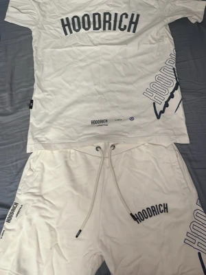 Vitt Hoodrich set med tryck - Säljer ett vitt set från Hoodrich med matchande t-shirt och shorts. Båda plaggen har svart Hoodrich-tryck och coola grafiska detaljer på både fram- och baksida. T-shirten har texten 'FROM NOTHING TO SOMETHING' och shortsen har dragsko i midjan. Perfekt för en avslappnad streetwear-look. T shirtenp passar som M och S. Pris kan diskuteras vid snabb affär.