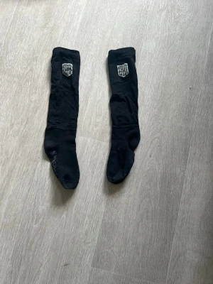 Svarta ridstrumpor från Maya Delorez - Säljer ett par svarta knähöga ridstrumpor från Maya Delorez. Strumporna har en vit logga upptill och texten 'MAYA DELOREZ' på foten. Perfekta till ridstövlar och sitter skönt på benet.