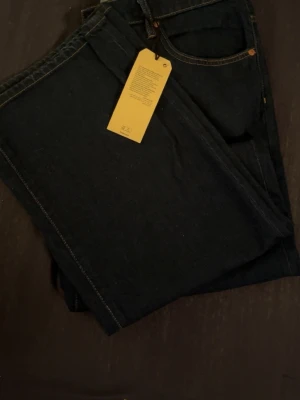 Mörkblå raka jeans med kontrastsömmar - Säljer helt nya oanvända snygga mörkblå jeans med klassisk femficksdesign och kontrastsömmar. Jeansen har raka ben och är tillverkade i ett robust denimtyg. Perfekta för dig som gillar en stilren och tidlös look.