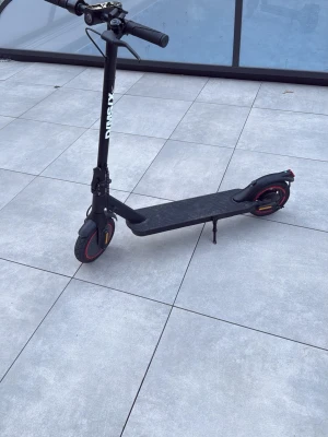 Svart elscooter med röda detaljer - Säljer en svart elscooter med röda detaljer på hjulen och reflexer. Scootern har bred fotplatta, handbroms, stöd och LED-belysning bak. Perfekt för att ta sig runt i stan på ett smidigt och miljövänligt sätt.