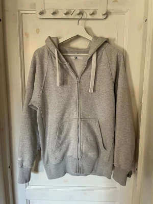Russemerch - Säljer en grå zip hoodie ifrån russemerch, stor huva och breda snören. Mjuk insida i fleece och två stora fickor framtill. Perfekt för chill dagar eller när du vill ha något bekvämt och enkelt. Klassisk passform och ribbade muddar vid ärmar och nederkant. Hör av dig vid frågor🙌🏼