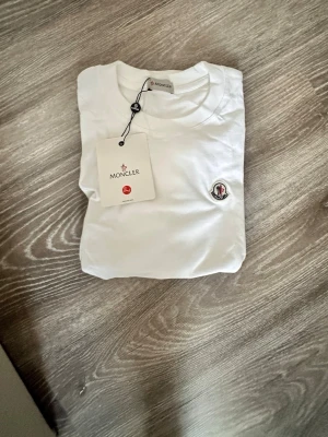 Vit t-shirt från Moncler - Snygg vit t-shirt från Moncler med klassisk rund hals och Moncler-logga broderad på bröstet. Tillverkad i mjuk bomull som känns skön mot huden. Enkel och stilren design som passar till det mesta.