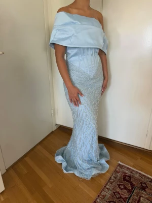 Ljusblå pärlbroderad maxiklänning / balklänning (off shoulder - Säljer min otroligt fina ljusblå klänning som endast är använd en gång. Klänningen har en elegant off shoulder-design, korsettdetaljer i midjan och ett vackert pärlbroderat nät över kjolen.   I mycket fint skick. En liten smutsfläck finns längst ner på insidan av fållen efter användning, men den syns knappt eftersom nätet faller över den lilla fläcken. Perfekt till bal, studentbal, gala eller fest.   Storlek = S/M   Genomskinlig shoulder band kommer dessutom med om man vill använda sig av det.  