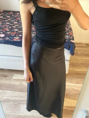 Svart långkjol i satin från Lindex - Säljer en svart långkjol i glansigt satinmaterial. Helt ny, prislapp sitter kvar. Nypris 399kr. Ej använd då den är för stor för mig