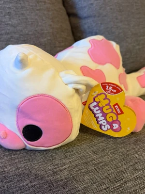 NY! ZURU Hug-A-Lumps 1,5kg Ko gosedjur - Supergulligt mjukisdjur från Zuru Hug a Lumps, formad som en ko med vit bas och rosa fläckar. Stora rosa och svarta ögon, mjuka öron och svans. Perfekt att krama och ha som dekoration eller gosedjur. Ny i kartong!