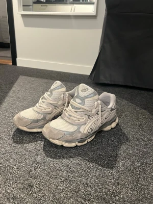 Beige Asics sneakers med mesh och mocka - Snygga beige sneakers från Asics med detaljer i mesh och mocka. Skorna har en chunky sula och klassiska Asics-stripes på sidan. Perfekta för dig som gillar sportig och trendig stil. Låga i modellen och med snörning framtill.