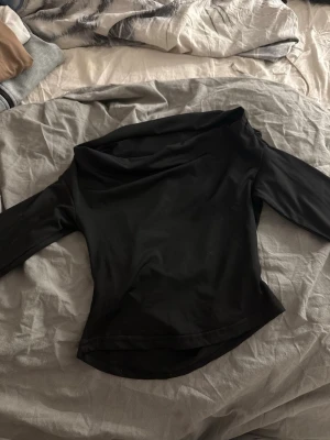 Svart offshoulder topp - Snygg svart offshoulder topp med trekvartsärm och en lätt glansig finish. Toppen har en draperad halsringning och sitter figurnära. Perfekt för dig som vill ha en stilren och trendig look.