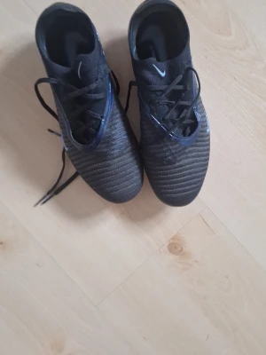 Svarta nike phantom 6 low elite - Andvänd 1 tränning man får även med påsen Säljer ett par svarta Nike fotbollsskor med vita detaljer och klassisk snörning. Skorna har dobbar för bra grepp på planen och är tillverkade i syntetmaterial med en sportig, strömlinjeformad design. Perfekta för dig som vill ta spelet till nästa nivå.