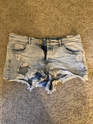 Ljusa slitna jeansshorts - ljusblå jeansshorts med råa kanter och slitningar framtill och baktill. Mycket strechigt matrial, passar alltså perfekt på kroppen. De är low waist också