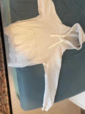 Ljusgrå hoodie med ficka och huva - Säljer en stilren ljusgrå hoodie med klassisk känguruficka och huva med snörning. Hoodien har långa ärmar och ribbade muddar vid ärmslut och nederkant. Perfekt för en avslappnad och bekväm look.