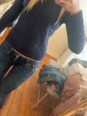 Mörkblå kabelstickad tröja Polo Ralph Lauren - Snygg mörkblå kabelstickad tröja från Polo Ralph Lauren med rund halsringning och ribbade muddar. Tröjan har den klassiska broderade loggan på bröstet och är gjord i mjukt material som sitter tajt och bekvämt. Perfekt till jeans eller kjol.