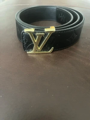 Snyggt svart bälte - Snyggt svart skärp med klassiskt spänne i guldmetall. Skärpet är gjort i exklusivt skinn och har diskret präglat monogrammönster längs hela bandet. Perfekt accessoar för att lyfta din outfit.