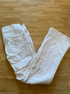 Vita jeans med broderad ficka  - Snygga vita jeans från lager 157 med broderad detalj på bakfickan och klassisk femficksmodell. Jeansen är bootcut och har dubbla knappar i midjan. Perfekta för dig som vill ha en clean och fräsch look. Den är i storlek xs short