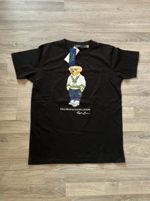 Svart Polo Bear t-shirt Ralph Lauren - Svart t-shirt från Ralph Lauren med ikoniska Polo Bear-trycket på bröstet. Klassisk rund hals och korta ärmar. Tillverkad i mjuk bomull för skön känsla. Perfekt för dig som gillar streetstyle och vill ha en tidlös look.