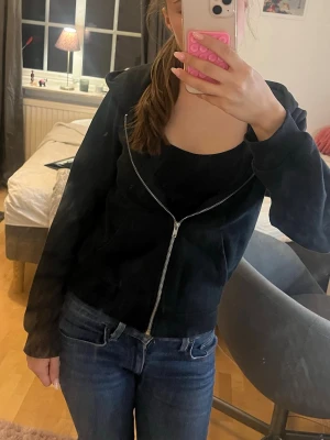 Svart zip hoodie med huva - Säljer en svart hoodie med dragkedja och huva. Hoodien har en klassisk passform, långa ärmar och en stor ficka framtill. Perfekt att slänga på sig över en t-shirt eller linne. Materialet känns mjukt och bekvämt, och den är enkel att matcha till olika outfits.