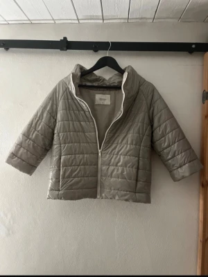 Grå pufferjacka - Stilren grå pufferjacka från LeMonada med quiltad design och hög krage. Jackan har trekvartsärmar och dragkedja framtill. Perfekt för dig som vill ha en lätt och trendig jacka till kyligare dagar.