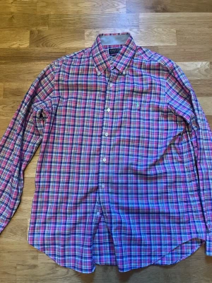 Rutig skjorta från Polo Ralph Lauren - Säljer en klassisk rutig skjorta från Polo Ralph Lauren i rosa, blått, vitt och grönt. Skjortan har lång ärm, knappar framtill och en liten broderad logga på bröstet. Perfekt för dig som gillar färg och tidlös stil.