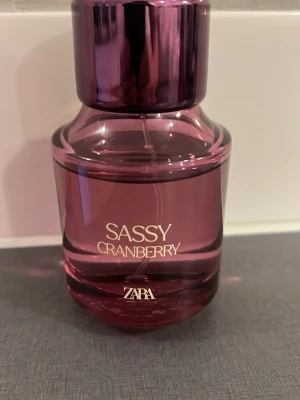 Zara Sassy Cranberry parfym - En snygg parfymflaska från Zara i modellen Sassy Cranberry. Flaskan är i en glansig, mörkrosa färg med rundad form och matchande lock. Perfekt för dig som gillar fruktiga och fräscha dofter med en hint av bär.