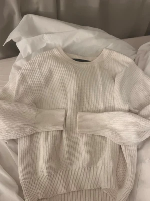 Vit ribbstickad tröja - Säljer en stilren vit ribbstickad tröja med rund hals och långa ärmar. Tröjan har breda muddar vid ärmslut och nederkant, vilket ger en snygg och avslappnad look. Perfekt att matcha med jeans eller kjol för en enkel men trendig outfit.
