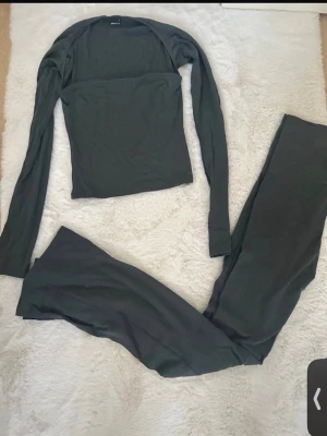 Mörkgrönt bodyset med lång ärm - Säljer ett mörkgrönt bodyset med långärmad topp och matchande byxa. Setet har en enkel, stilren design och är tillverkat i ett mjukt, stretchigt material som sitter skönt mot kroppen. Perfekt för dig som gillar minimalistisk stil.