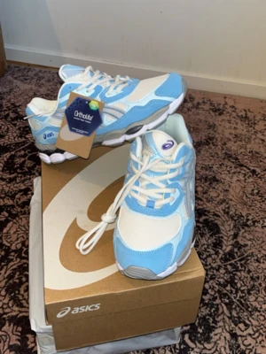 ASICS blåvita sneakers med mesh, helt nya - Fräscha sneakers från ASICS i en snygg kombination av ljusblått, vitt och grått. Skorna har klassisk låg profil, meshpaneler för extra andningsförmåga och detaljer i syntetmaterial. Perfekta för dig som gillar sportig och trendig stil.