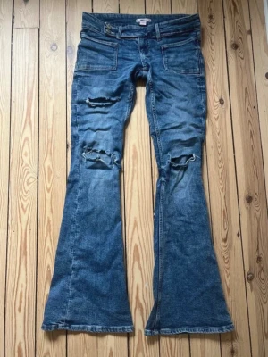 Blå bootcut jeans från Gina Tricot 14+ - Bootcut jeans i blå denim från Gina Tricot med slitna detaljer på knäna och framsidan. Jeansen har två stora framfickor, och de inna hållet har blivit lite uttöjt och lite liksom slitet  men är mycket bra skick, det är i 14+ tall