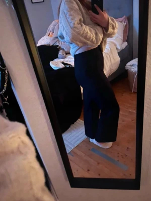 Svarta vida kostymbyxor - Säljer ett par svarta kostymbyxor med hög midja och vida ben. Byxorna har en klassisk look och är perfekta för en stilren outfit. Materialet ser ut att vara vävt tyg som ger en snygg och dressad känsla. Säljer även topparna i mitten bilderna! 