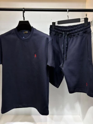 Mörkblått set Ralph Lauren - Snyggt mörkblått set från Polo Ralph Lauren med t-shirt och shorts. Båda plaggen har den klassiska röda logotypen broderad på bröstet respektive benet. Setet har en enkel och stilren design med rund halsringning och dragsko i midjan på shortsen. Perfekt för en avslappnad look.
