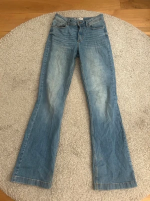 Ljusblå bootcut jeans från jdy  - Säljer ett par ljusblå bootcut jeans från jdy med klassisk femficksdesign och lätt slitna detaljer framtill. Jeansen har normal midja och utsvängda ben, perfekta för en avslappnad och trendig look.