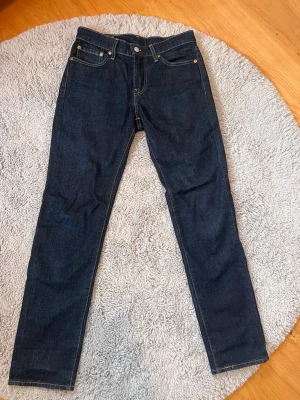 Mörkblå Levi's 511 jeans - Säljer ett par mörkblå Levi's 511 jeans i klassisk slim fit-modell. Jeansen har fem fickor, gul kontrastsöm. Jeansen har aldrig används och har alltså inga hål eller slitningar! De är i storlek W29 L32. Går absolut att diskutera priset!